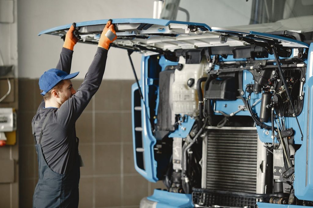 Mechanic in uniform inspecting truck engine for maintenance indoors.